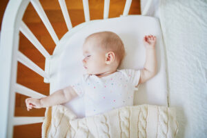 Adorable baby girl sleeping in co-sleeper crib attached to parents' bed. Little child having a day nap in cot. Sleep training concept. Infant kid in sunny nursery
